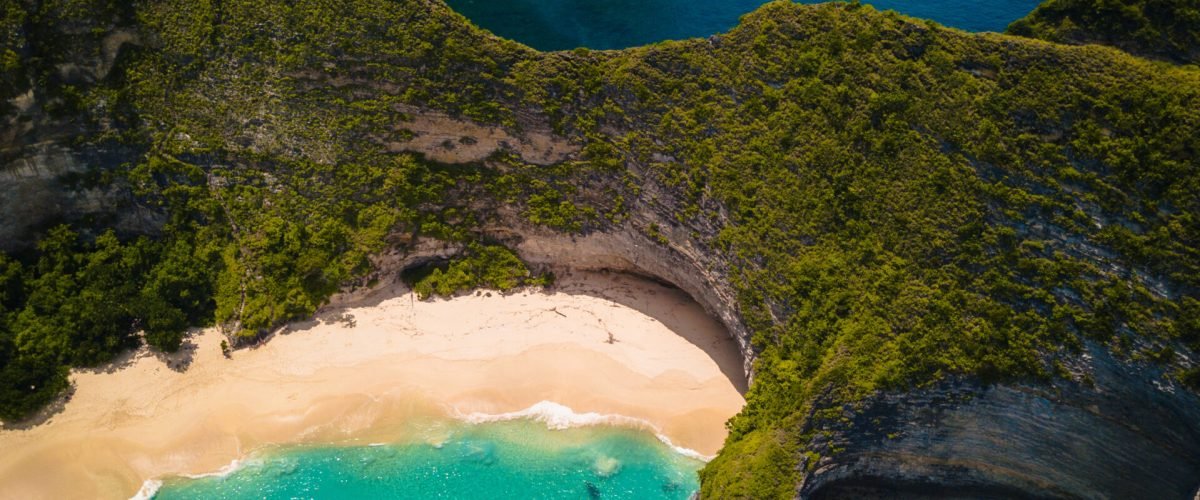 An aerial shot of the ocean  surrounded by beautiful cliffs covered in greens