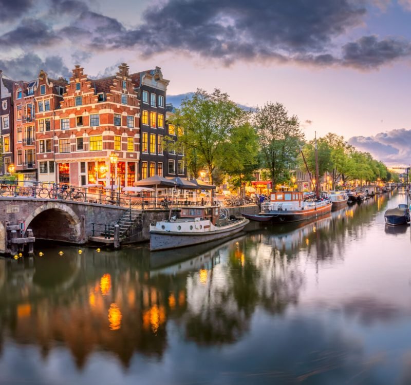 Amsterdam. Panoramic view of the downtown of Amsterdam. Traditional houses and bridges of Amsterdam. A blue evening time and the serene reflection of lights in the water. Long exposure. A European journey to a historic city. Europe, Netherlands, Holland, Amsterdam.